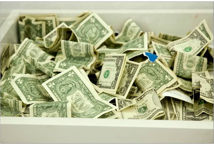 A white box overflowing with crumpled one dollar bills.. Text: ONE
