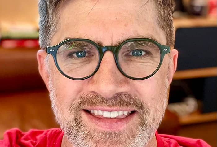 A close-up photo of a man with glasses smiling at the camera.