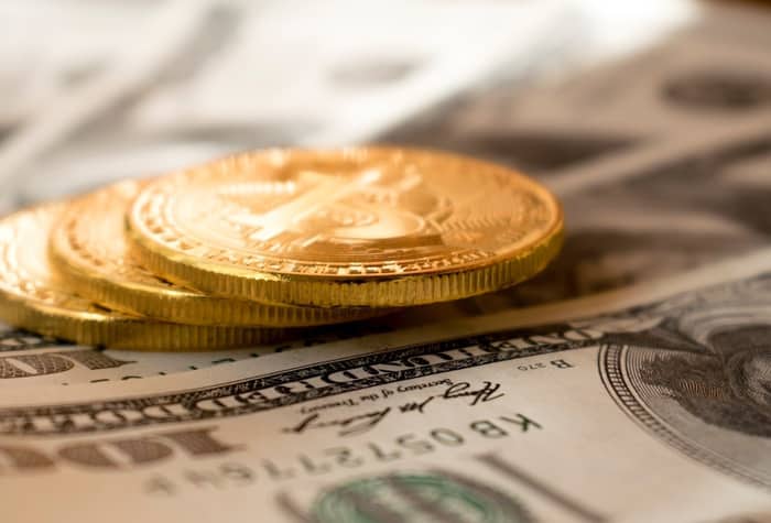 Three gold coins rest on top of a blurred background of US dollar bills.