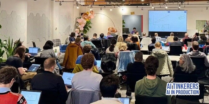(Photo) A group of people are sitting in a room, looking at a presentation on a large screen. They appear to be attending a workshop or conference, with many using laptops. Text: AI TINKERERS AI IN PRODUCTION people | indoor | presentation, laptops, group of people | candid Note: The image is a real-life captured scene of an event, showing people and a presentation, making it a photograph.