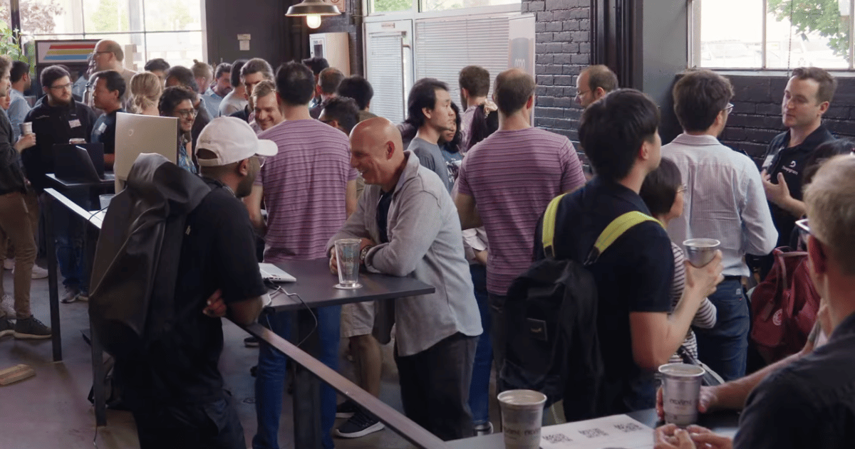 (Photo) A photo of a crowd of people gathered in an indoor space, possibly a conference or networking event. people | indoor | crowd, social interaction | candid Note: The image is a real-life captured scene of people in a social/professional setting, indicative of a photograph.