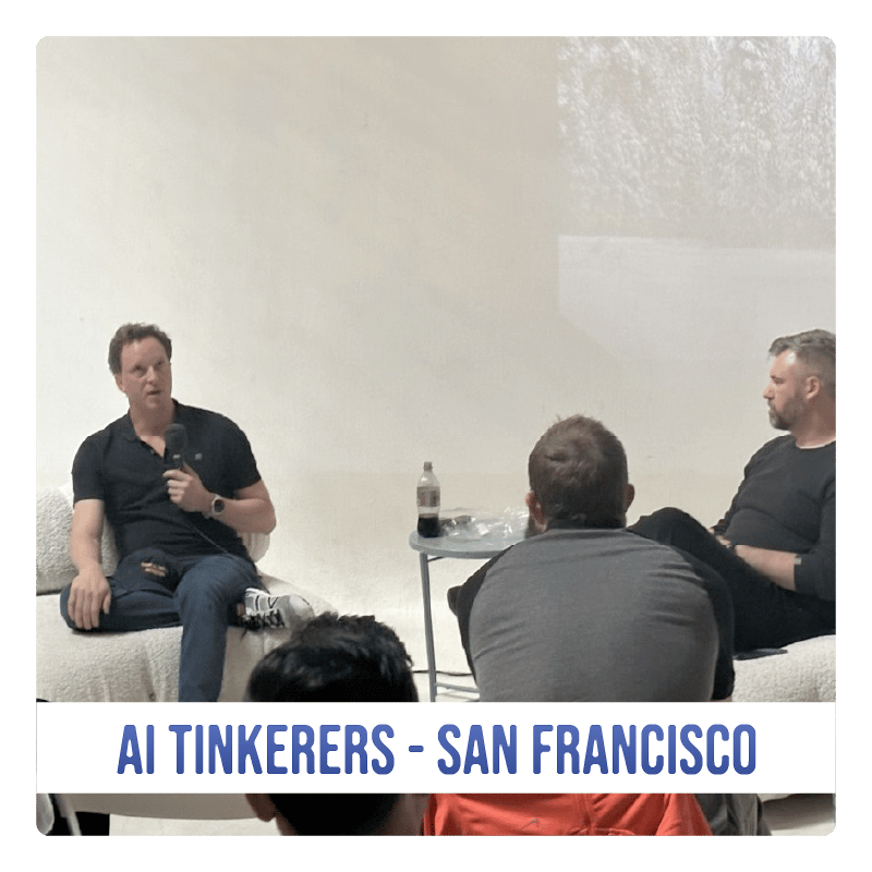 (Photo) A photo of a man speaking to a small audience in a casual setting. The event appears to be related to AI Tinkerers in San Francisco. Text: AI TINKERERS - SAN FRANCISCO people | indoor | small group, presentation | candid Note: The image is a real-life captured image of people in a room, making it a photograph. The added text banner further suggests it's documenting an event.