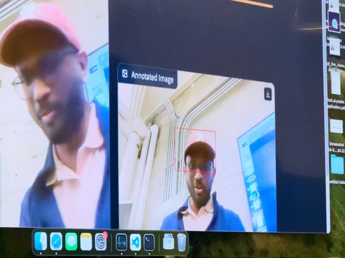 (Photo) A screenshot of a computer screen displaying a video conferencing call with a man wearing a pink baseball cap and glasses. Text: Annotated Image person | indoor | video conference, computer screen | candid Note: The image is a photograph of a computer screen showing a video call, which falls under the category of a photo.  It captures a real-life scene rather than a designed graphic or illustration.