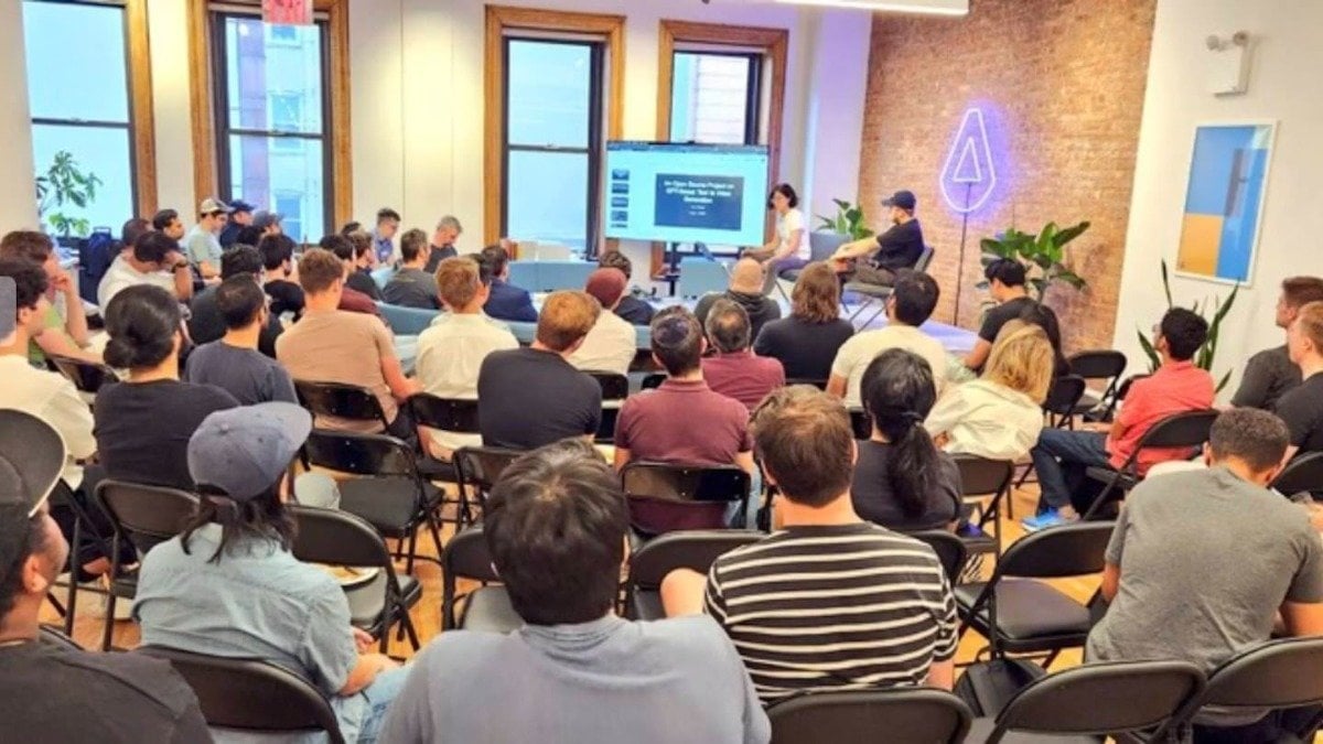 (Photo) A group of people are sitting in chairs facing a presentation screen and two presenters. Text: How Open Source Projects Grow from 0 to 1 Million Downloads people | indoor | presentation, audience, presenters | candid Note: The image is a real-life capture of an event, depicting a presentation and an audience.  This clearly falls under the category of a photograph.
