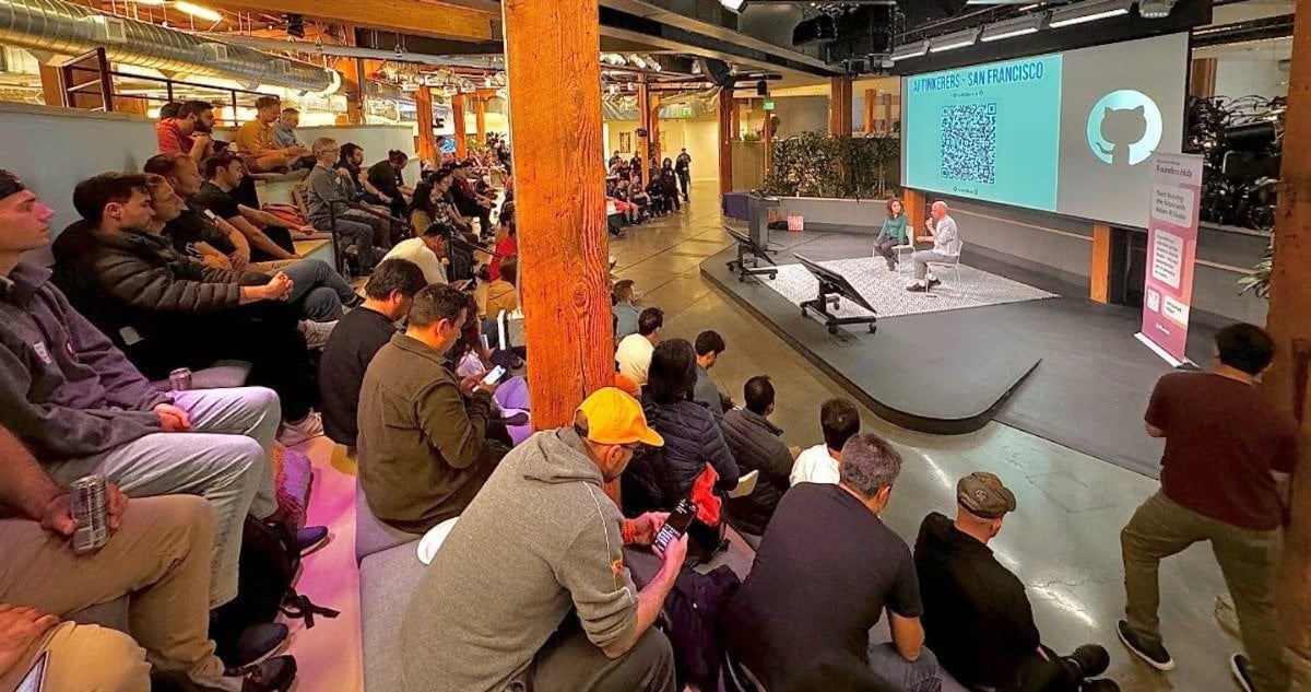 (Photo) A photo of an audience watching a presentation in a large, modern space. Two presenters are on a stage in front of a large screen displaying a QR code and a logo. Text: #Auth0USERS - SAN FRANCISCO people | indoor | presentation, audience, stage, screen | candid Note: The image is a real-life capture of an event, depicting people and a presentation setting.  It's not a drawing, logo, or banner itself.