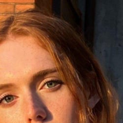 (Photo) A close-up photo of a person with light skin, freckles, green eyes, and reddish-blonde hair. person | outdoor | freckles, green eyes | portrait | Colors: #eeb49f, #a77560, #506040 Note: The image is a realistic depiction of a person's face, captured through photography.  There are no drawn or graphic elements.