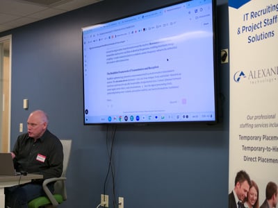 A man is giving a presentation in an office setting, with a large screen behind him displaying a document about signal processing and Buddhist philosophy.