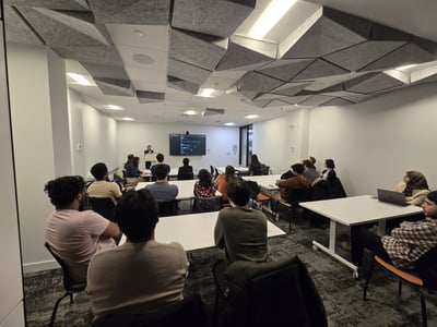 A group of people attending a presentation or workshop in a modern room with distinctive geometric acoustic ceiling panels.