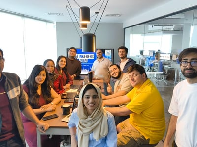 A group of eleven people, likely team members or colleagues, are gathered around a conference table in a bright, modern office space, posing and smiling for a group photo.