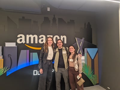 Three people posing together in front of an Amazon city skyline backdrop.