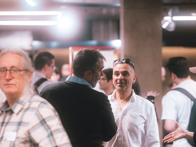 A candid photograph of people socializing and talking at an indoor networking event.