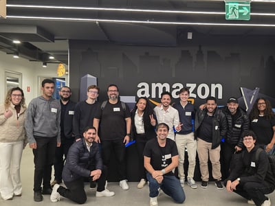 A group of colleagues posing together for a photo in front of a wall featuring the Amazon logo inside an office building.