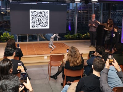 A robotic dog performs on a small stage in front of an audience, while a large screen behind it displays a prominent QR code.