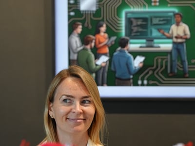 A portrait of a smiling woman standing behind a blurred pile of red plush toys, with a screen in the background displaying an 'AI Tinkerers - Seattle' graphic.