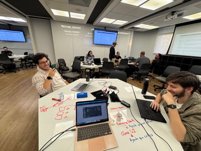 A group of people are working and collaborating in a modern office or coworking space, with diagrams and notes written directly on one of the white tables.