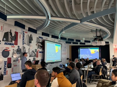 A group of people are gathered in a modern office space for a presentation titled 'Sundial Claw & Software Factories'. The room features a distinctive curved ceiling and a wall decorated with a timeline of tech companies.
