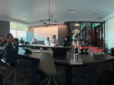 A group of people are gathered in a modern conference room for a presentation, with a man on the right gesturing towards a large screen showing 'Input Gateway'.