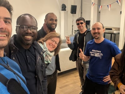 A diverse group of seven people are smiling and posing for a selfie-style photo in an indoor setting.