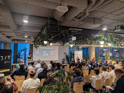A presenter stands before a seated audience in a modern office space, delivering a presentation on the automotive parts market landscape.