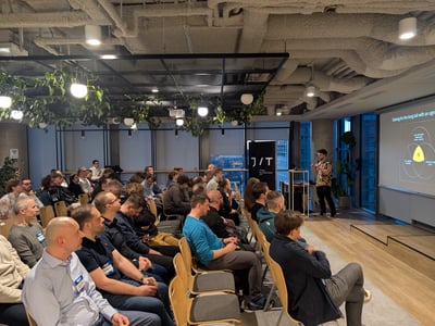 A speaker delivers a presentation about AI agents to a seated audience in a modern, industrial-style office space.