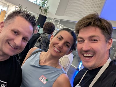 A cheerful selfie of three people smiling at an indoor networking event, with others visible in the background of the modern venue.