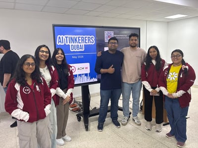 A group of seven people posing for a photo in front of a large digital screen displaying event information.