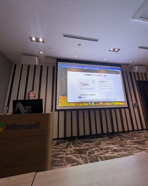 A presenter stands behind a Microsoft-branded podium next to a large projection screen displaying a presentation titled 'XINNI'S LIFE OS'.