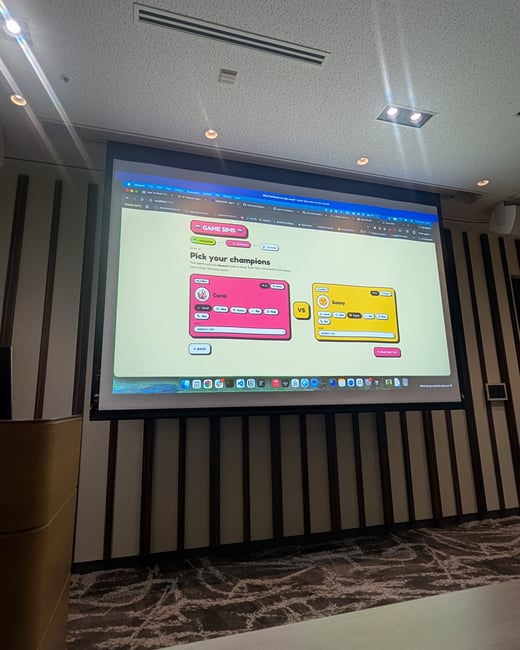A photograph of a large projection screen in a conference room displaying a game setup interface.