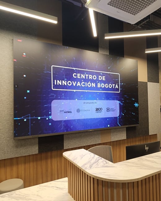 A large digital screen in a modern office or reception area displays 'CENTRO DE INNOVACIÓN BOGOTÁ' above a marble-topped counter.