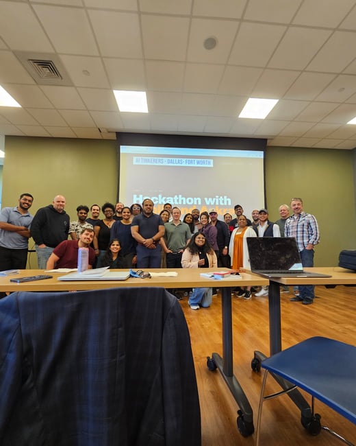 A group of approximately twenty-one people posing for a group photo in a classroom or conference room setting, with a presentation screen in the background.