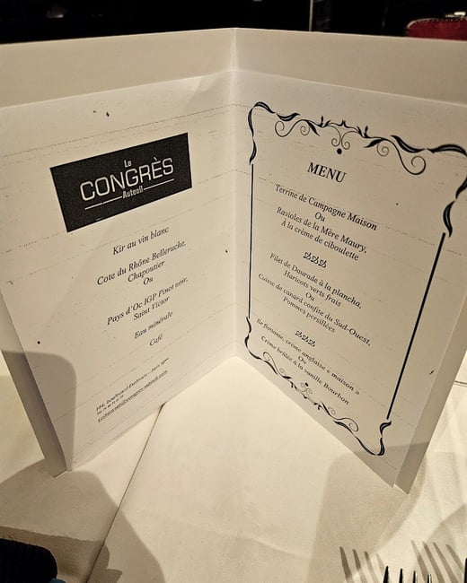 A close-up photograph of an open, bi-fold restaurant menu for "Le Congrès Auteuil" resting on a white tablecloth, listing French dishes and drinks.