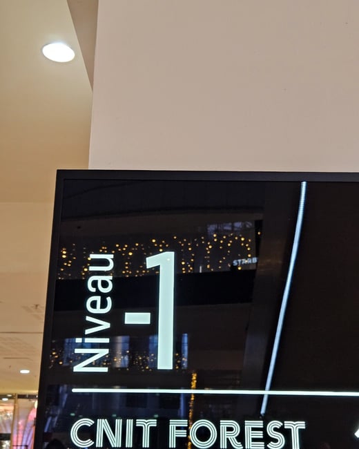 A close-up photograph of a modern, high-contrast illuminated sign inside a building, displaying the level designation "Niveau -1" and the destination "CNIT FOREST".