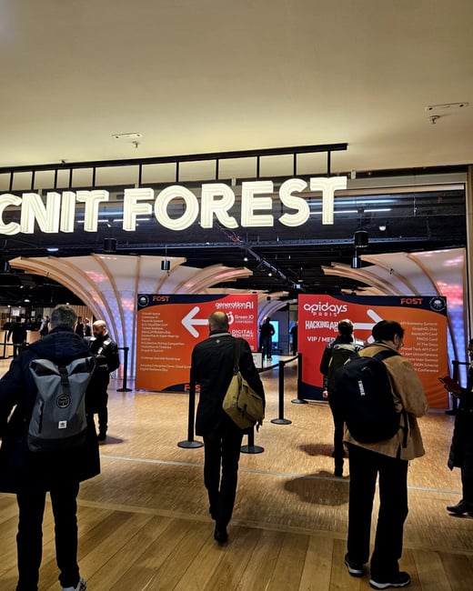 A photograph capturing the brightly lit entrance to the "CNIT FOREST" event space at a convention center, flanked by large banners advertising technology conferences like "generationAI" and "apidays," with several attendees walking toward the entrance.