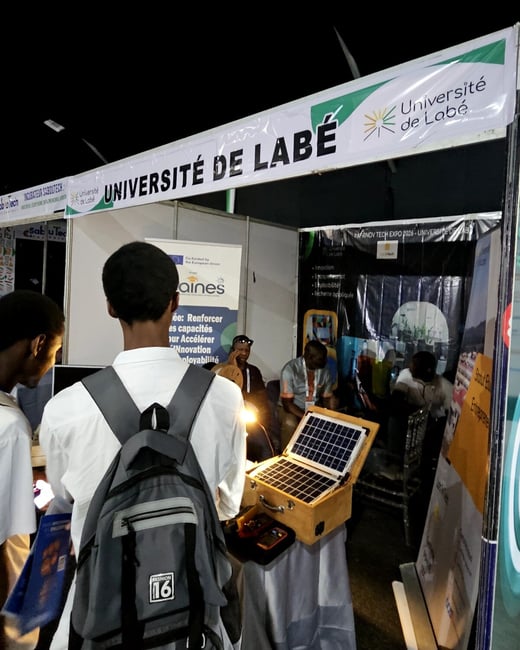 A university exhibition booth for the Université de Labé at a tech expo, featuring a solar panel demonstration and several attendees.