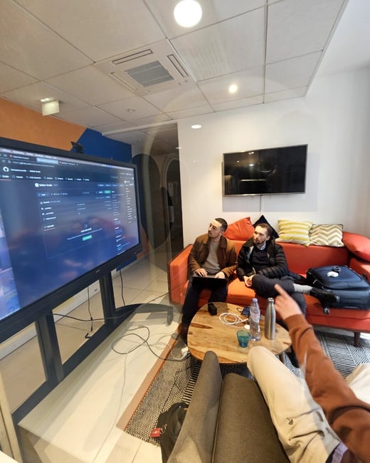 A group of people in a modern office space are looking at a large screen displaying a GitHub repository, likely during a demo or collaborative session.