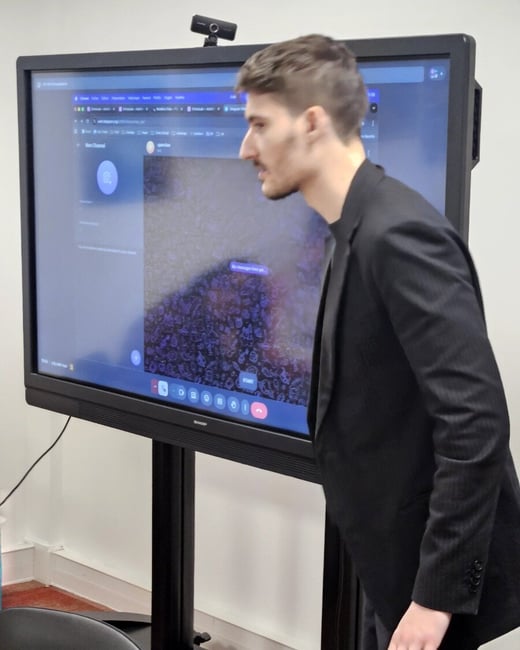 A man in a black suit stands in profile, looking closely at a large SHARP interactive display showing a digital interface.