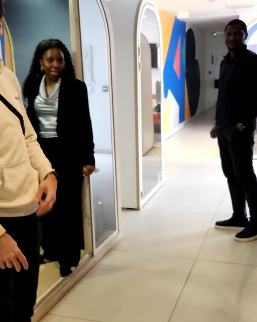 A photograph showing three people in a modern office hallway featuring arched doorways and colorful wall graphics.