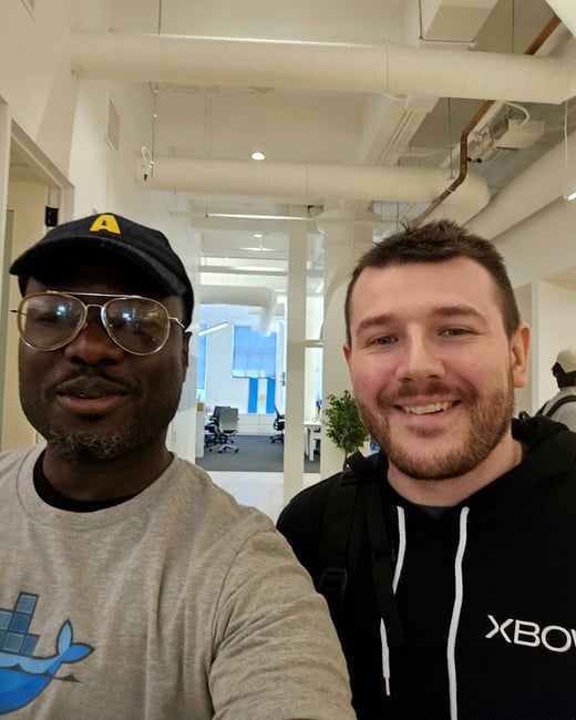 A selfie of two men standing in an office hallway, with one man wearing a Docker t-shirt and the other an Xbox hoodie.