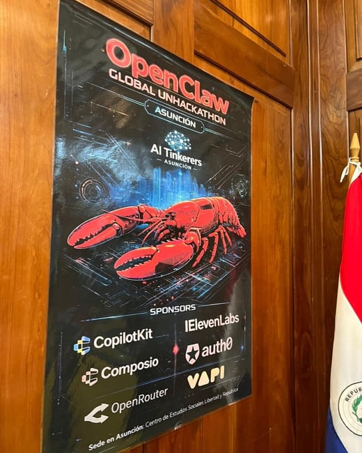A photograph of a promotional poster for the 'OpenClaw Global Unhackathon' in Asunción, mounted on a wooden wall next to a Paraguayan flag.