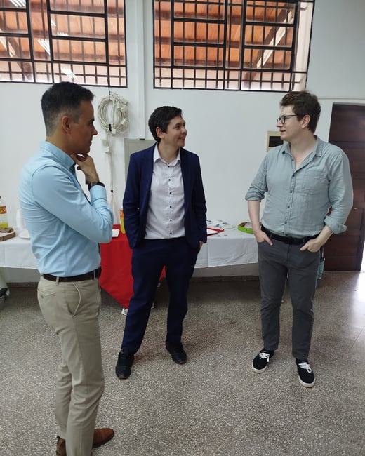 Three men in business casual attire are standing in a room and having a conversation.