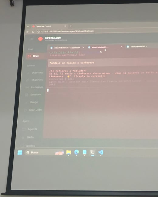 A photograph of a projection screen in a room, displaying a web-based software dashboard called 'OpenClaw' with a chat interface in Spanish.