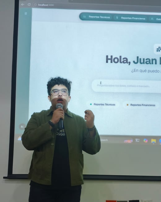 A young man is giving a presentation in front of a projector screen, holding a microphone and gesturing with his hand.