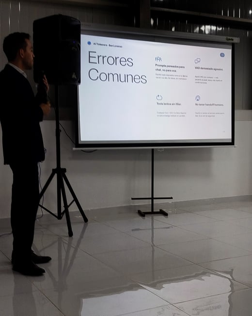 A man in a dark suit stands next to a large projector screen delivering a presentation in Spanish titled 'Errores Comunes'.