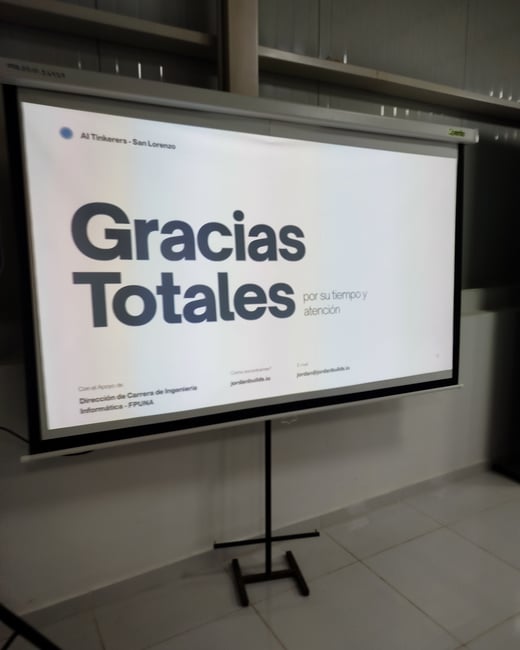 A photograph of a projector screen on a stand displaying a presentation slide with the words 'Gracias Totales' in Spanish.