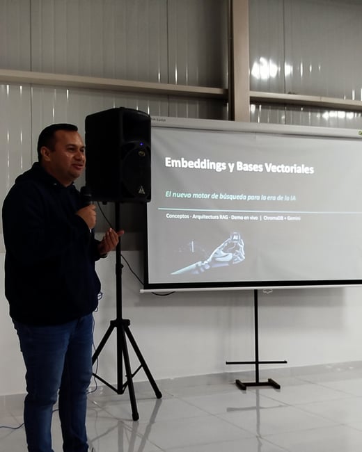 A man stands indoors holding a microphone, giving a presentation next to a projector screen displaying a slide about embeddings and vector databases.