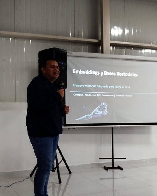 A man stands presenting in front of a projection screen displaying a slide about vector databases and embeddings in Spanish.