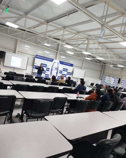 An indoor photograph of a presentation or lecture taking place inside a university hall, with a speaker presenting in front of banners for the Universidad Nacional de Asunción.