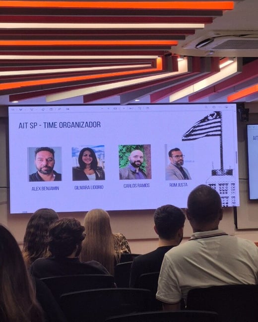 A photograph of a presentation screen showing four individuals titled 'AIT SP - TIME ORGANIZADOR' with an audience seated in the foreground.