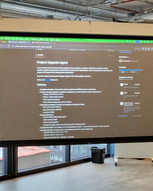 A photograph of a large screen in an office setting displaying a GitHub README page for a software tool called 'Project Upgrade Agent'.