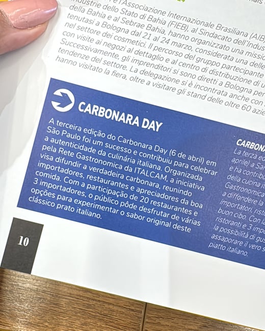 A close-up photograph of a person's hand holding open a magazine page featuring an article about 'Carbonara Day'.
